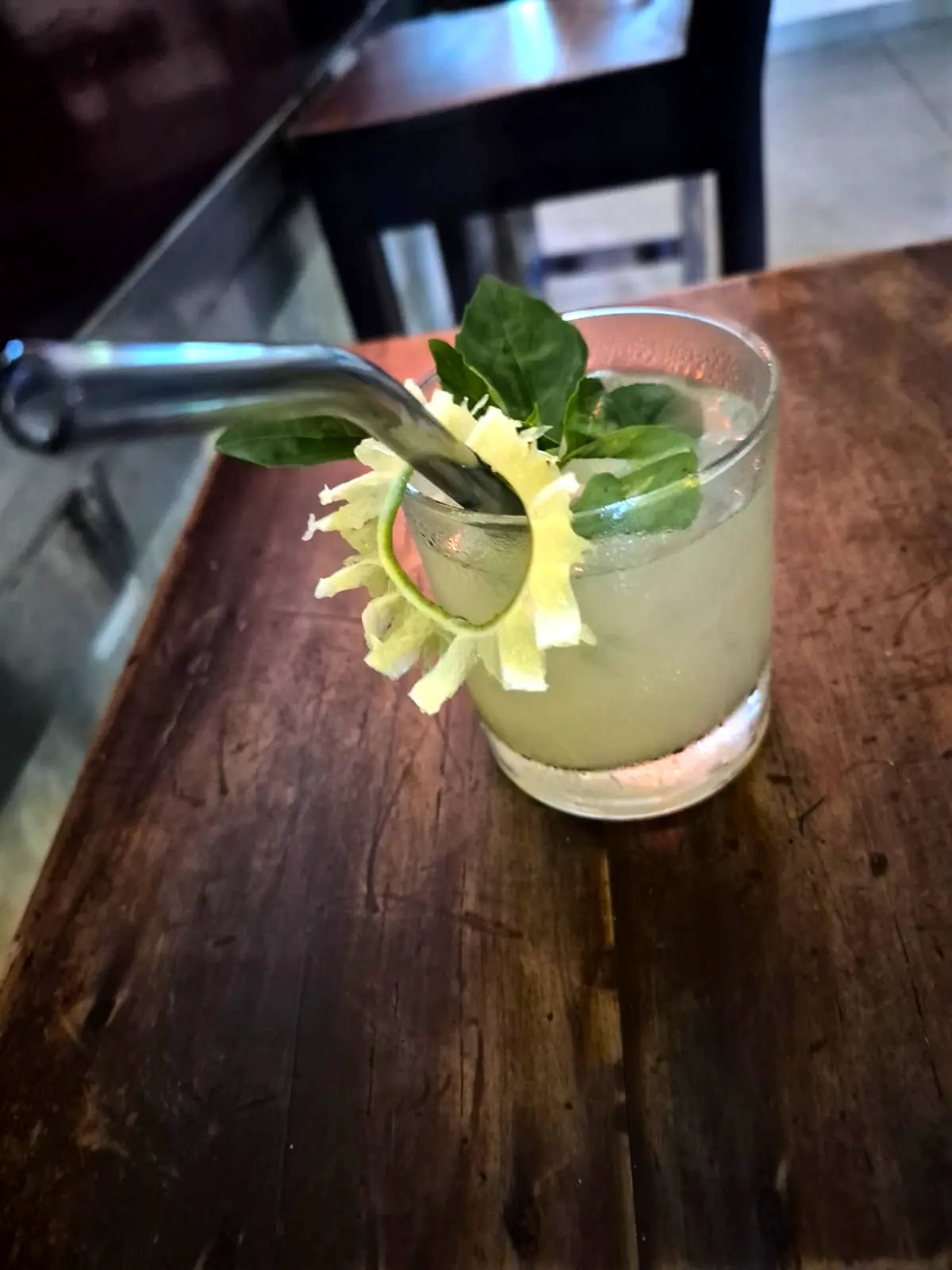 A lime and mint cooler garnished with a cucumber spiral on a dark wooden table