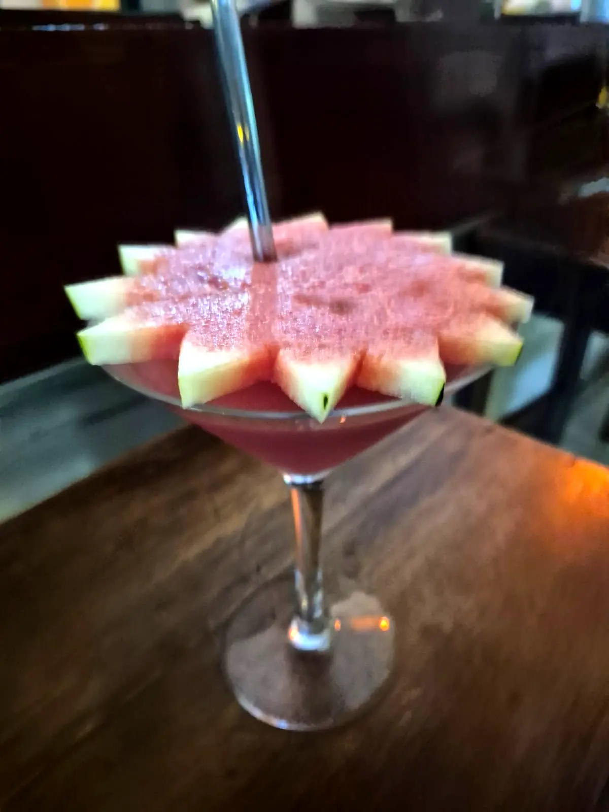 A pink watermelon cocktail in a martini glass, rimmed with watermelon slices