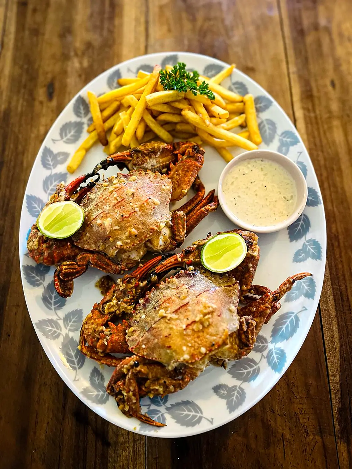 Two whole crabs with chips, lime wedges and garlic sauce on a blue-patterned plate