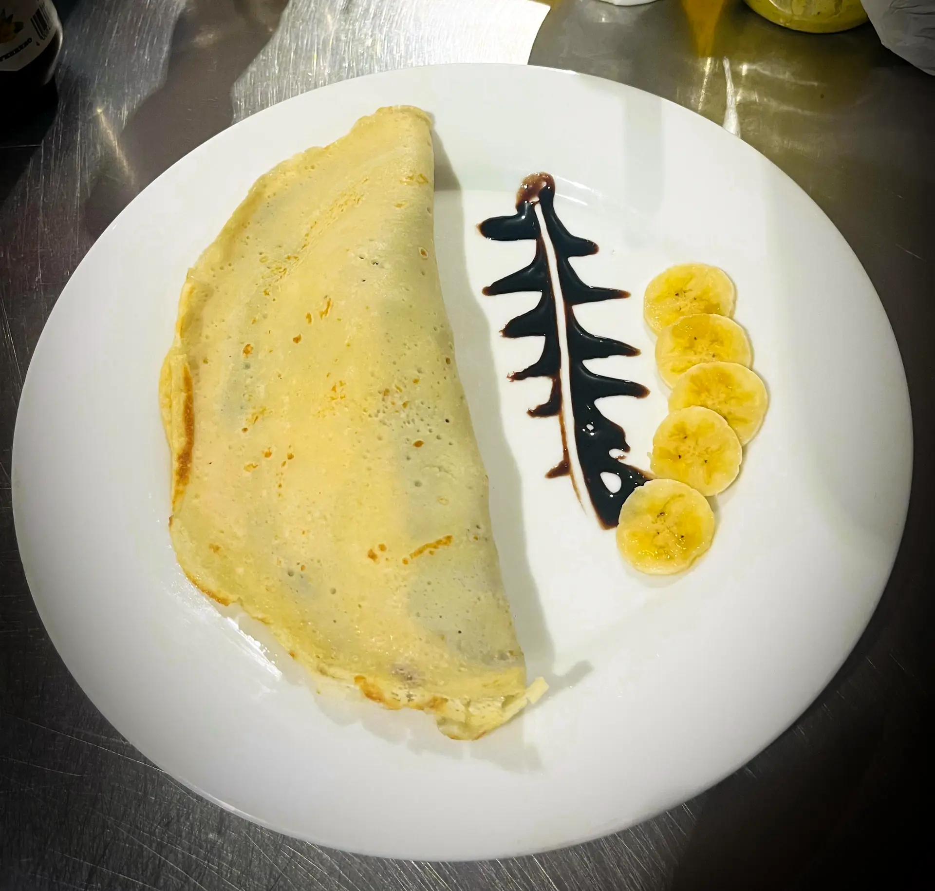 A folded pancake with sliced banana and a chocolate drizzle