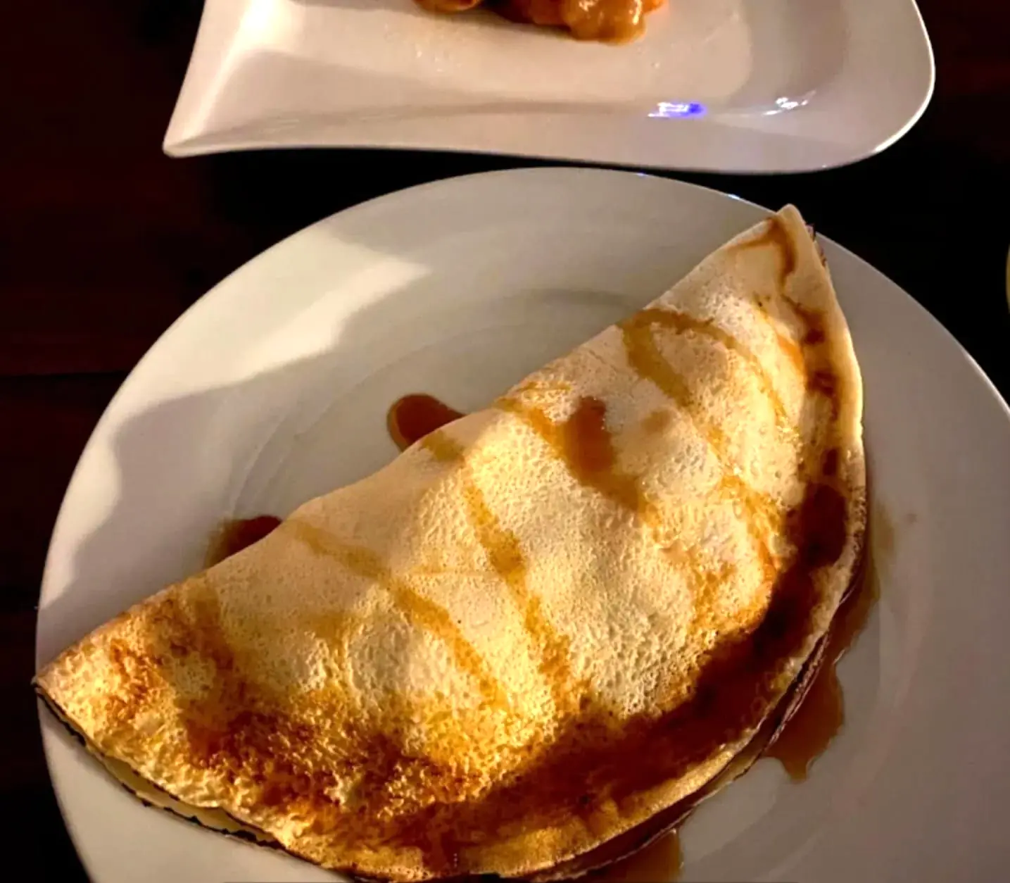 A golden pancake folded on a plate with caramel sauce