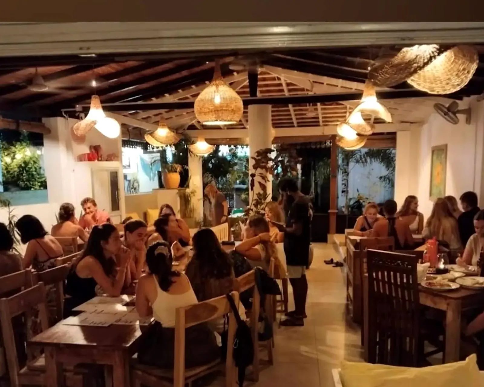 A full dining room at Pink Elephant on a weekday evening, with guests at long wooden tables under rattan lamps