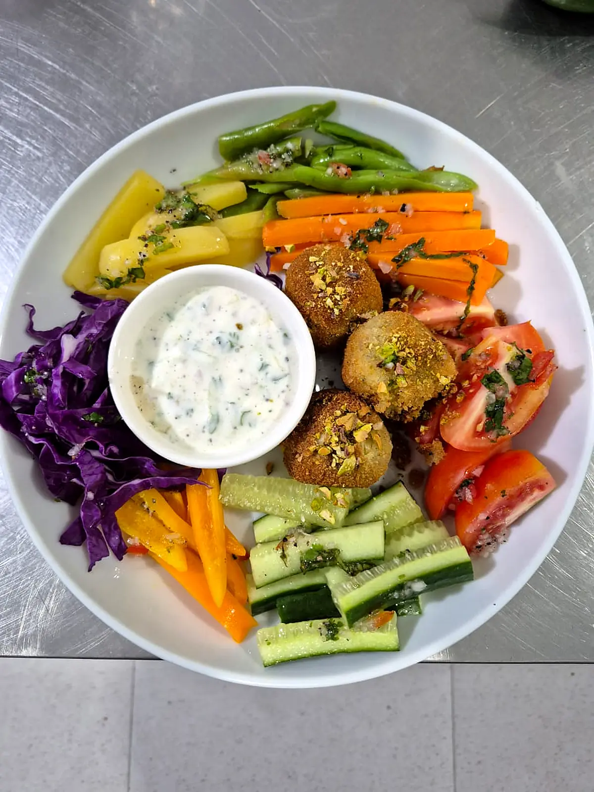 Falafel with yoghurt dip, red cabbage, carrots, beans and tomatoes on a round plate