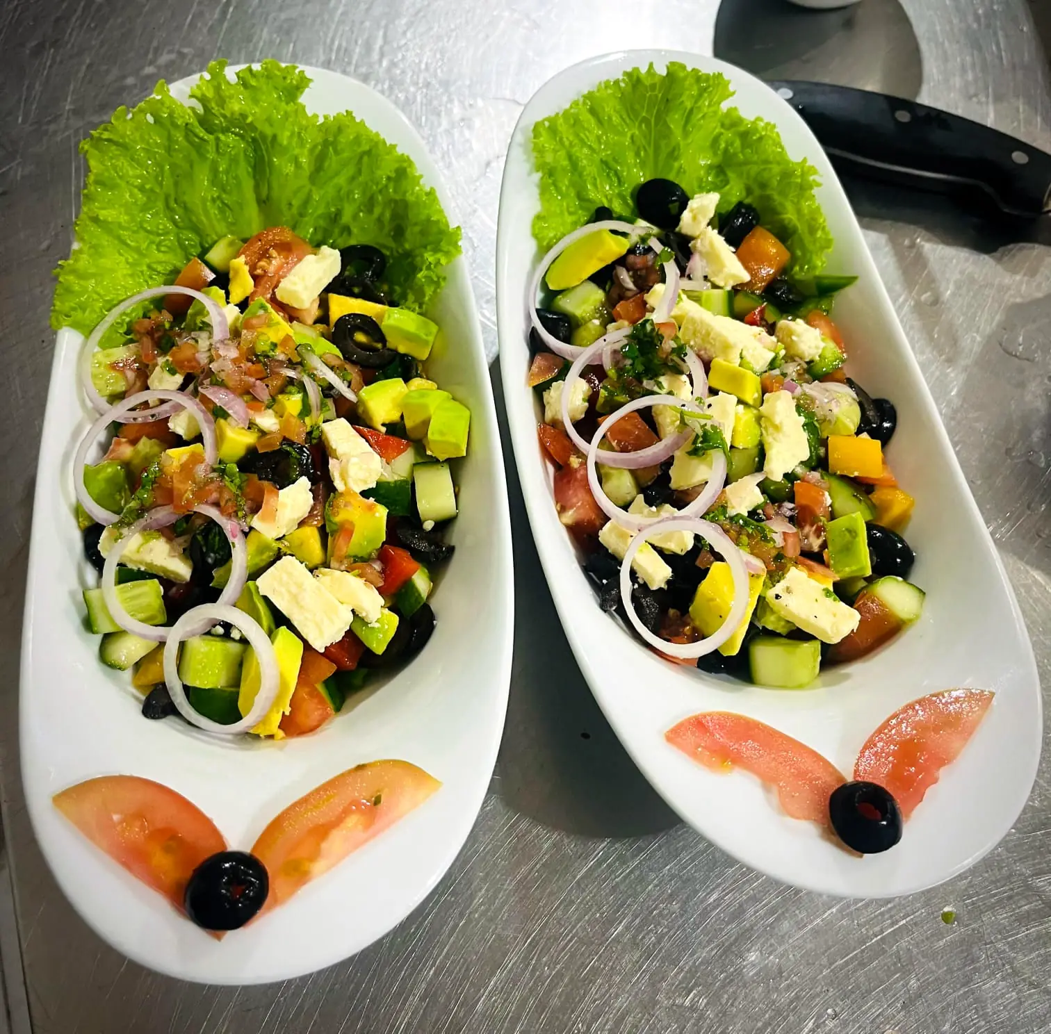 Two Greek-style salads with feta, olives, cucumber and tomato in white boat-shaped dishes