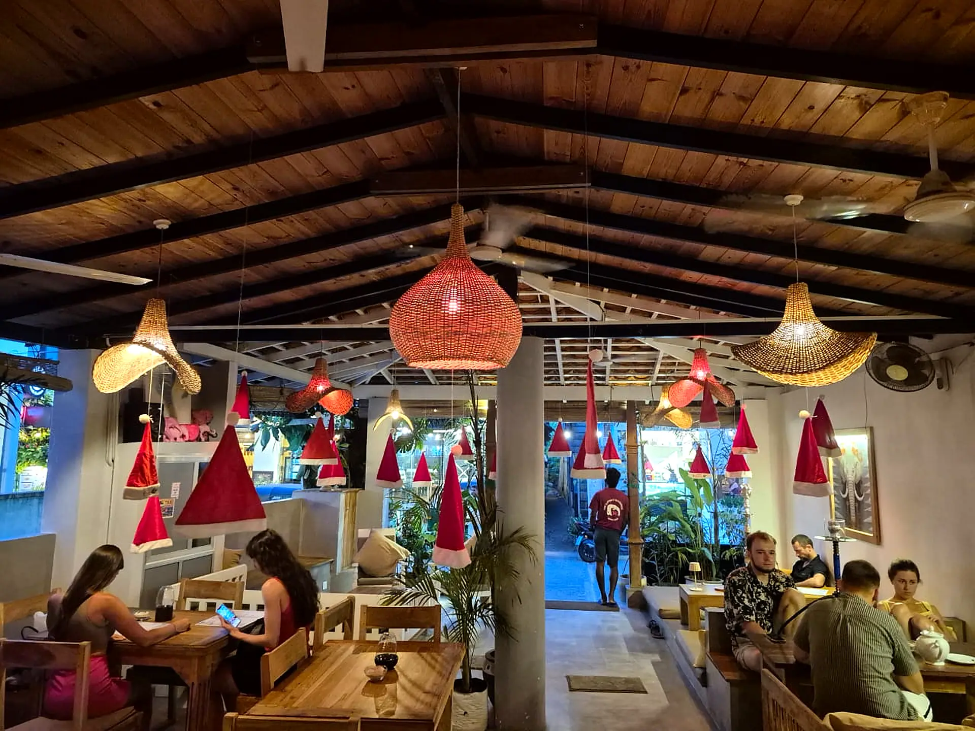 The open-sided dining room at Pink Elephant in the evening, with woven lanterns, timber roof beams and diners at wooden tables