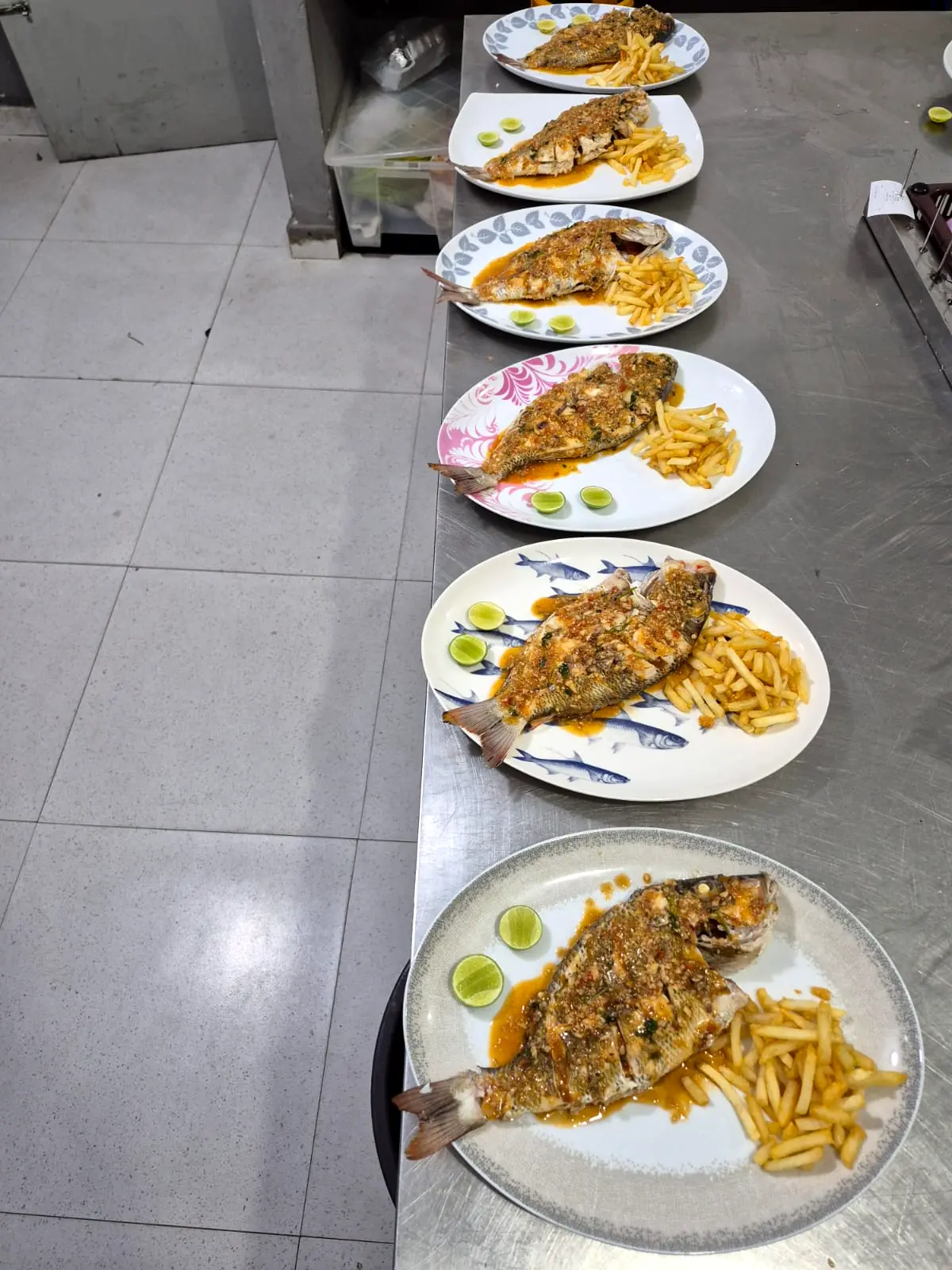 Six plates of whole fried fish with chips lined up on the kitchen pass, ready to go out