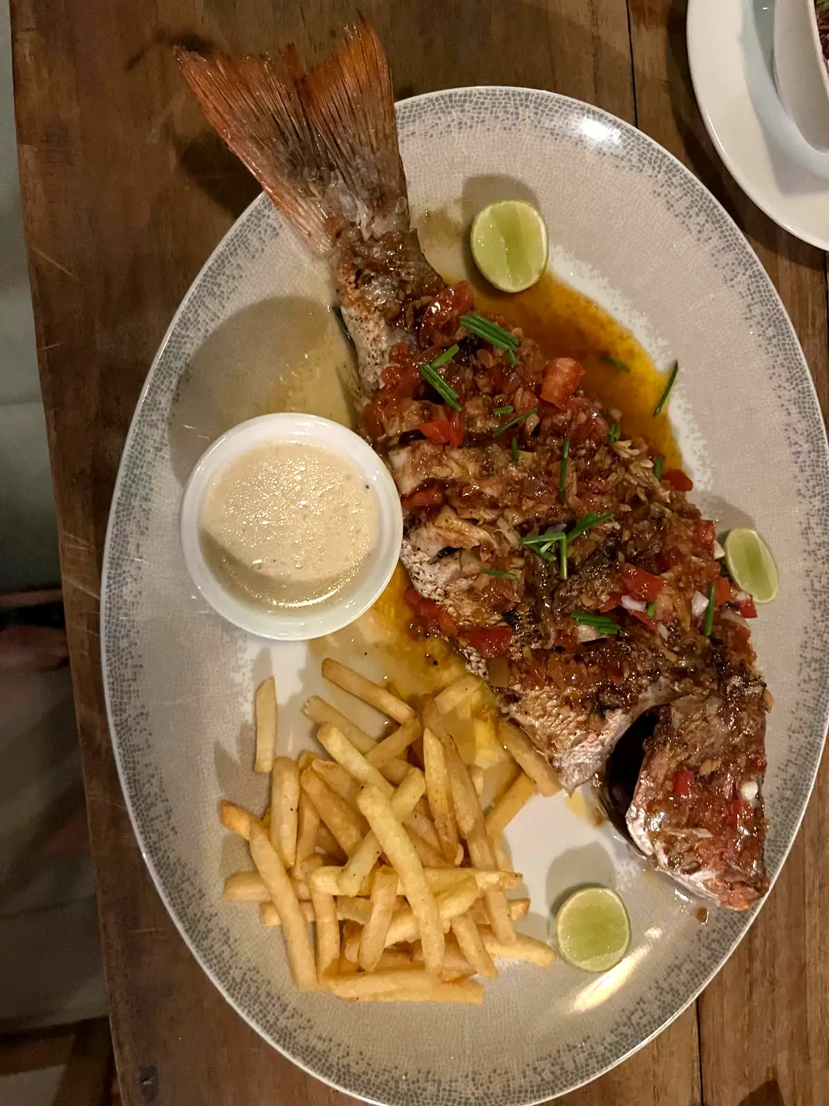 Whole red snapper with chips, lime and a dipping sauce on a white platter