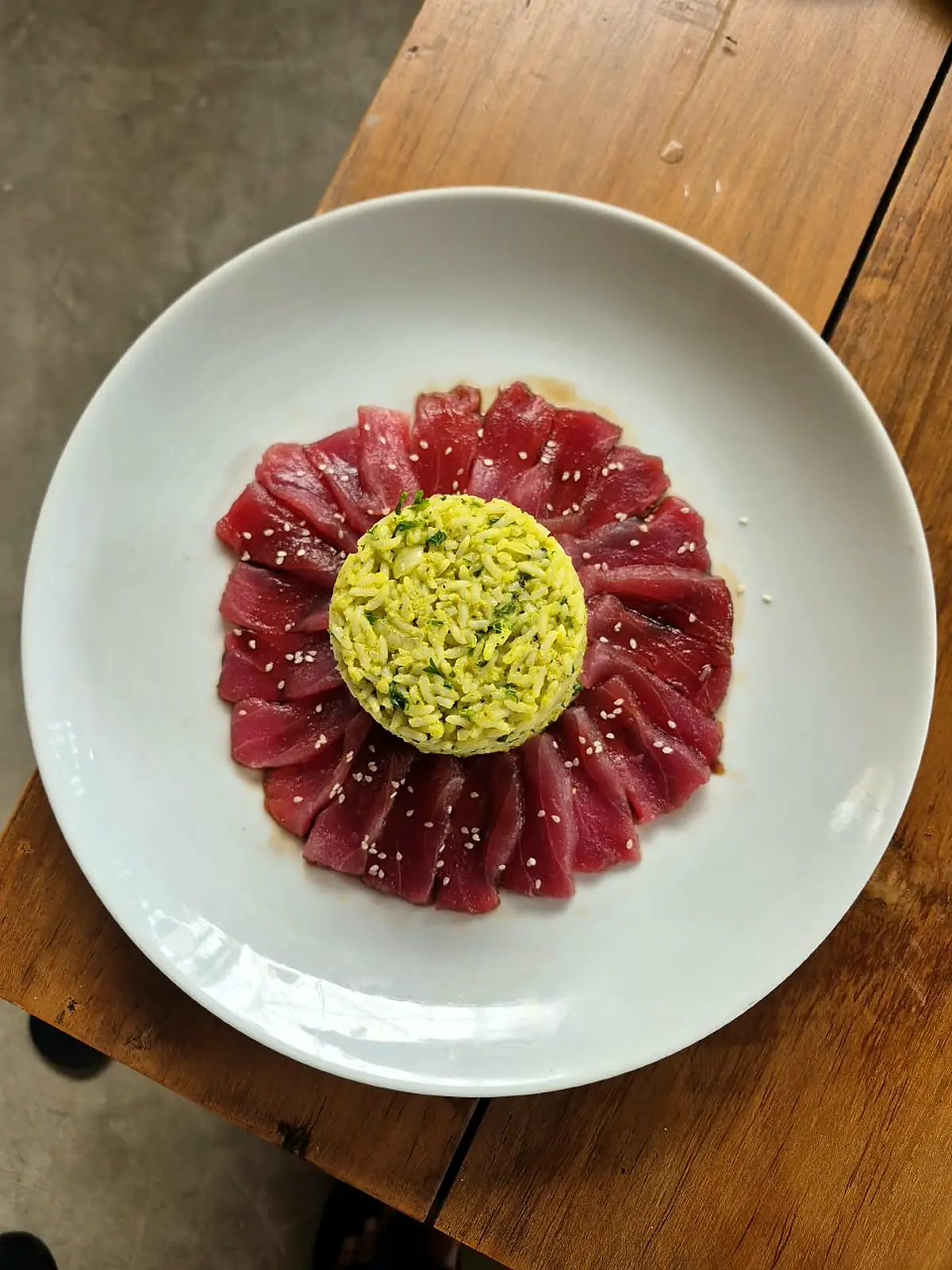 Thinly sliced raw tuna fanned around a mound of avocado on a white plate